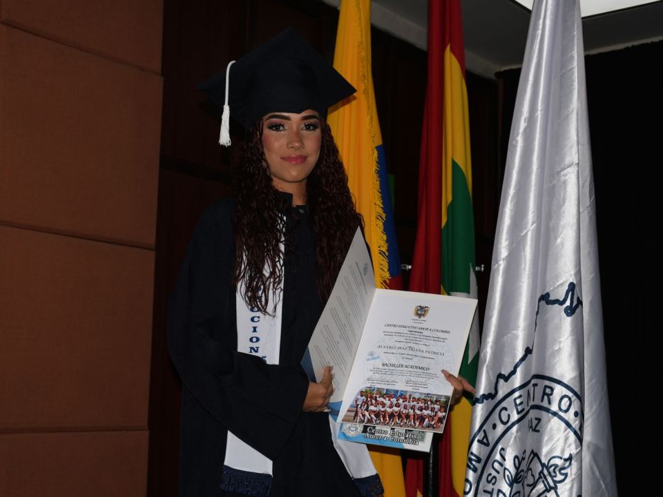 Graduada del CEAC mostrando su diploma de Bachiller Académico, junto a la bandera del colegio